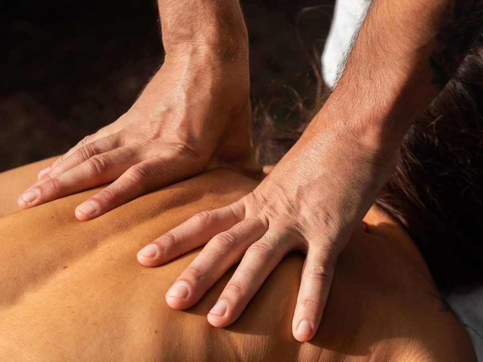 Zwei Hände drücken mit offenen Handflächen auf den Rücken einer liegenden Person, bei einer Deep-Tissue-Massage